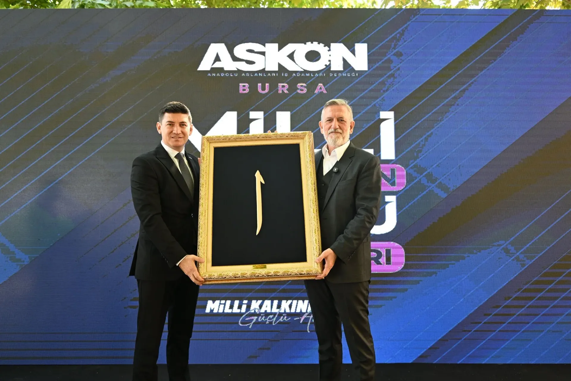 BTSO Başkanı İbrahim Burkay ile ASKON Bursa Şubesi Başkanı Emre Yıldız, Milli Kalkınmanın Güçlü Buluşmaları programında hediye takdimi sırasında
