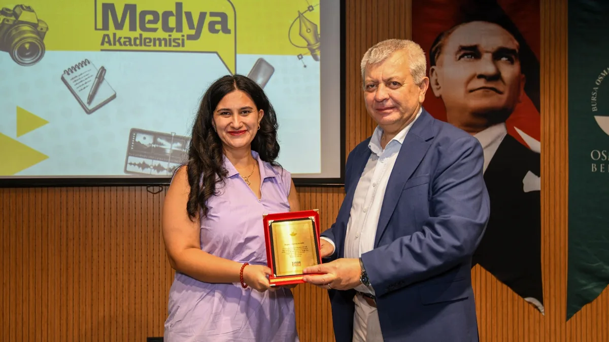 Osmangazi Medya Akademisi sertifika töreninde akademiye katkı sunan bir konuğa teşekkür plaketi takdim edilirken.